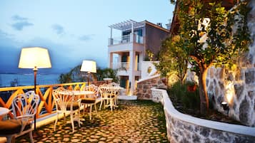 Una terraza con suelo de piedra, mobiliario exterior y vista al mar.