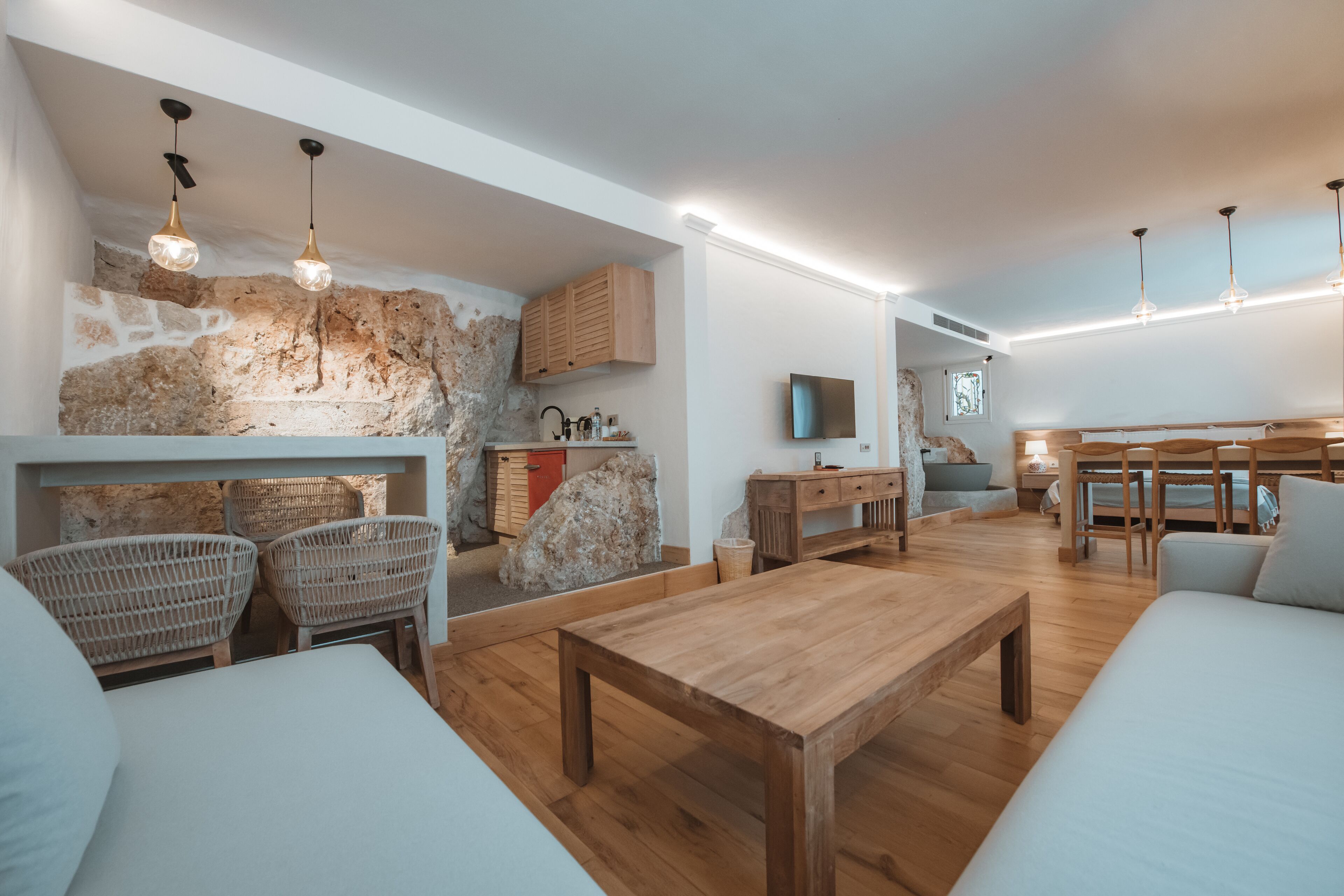 Ein modernes Wohnzimmer mit Steinwand, Holzmöbeln, Korbstühlen und einem Holztisch.