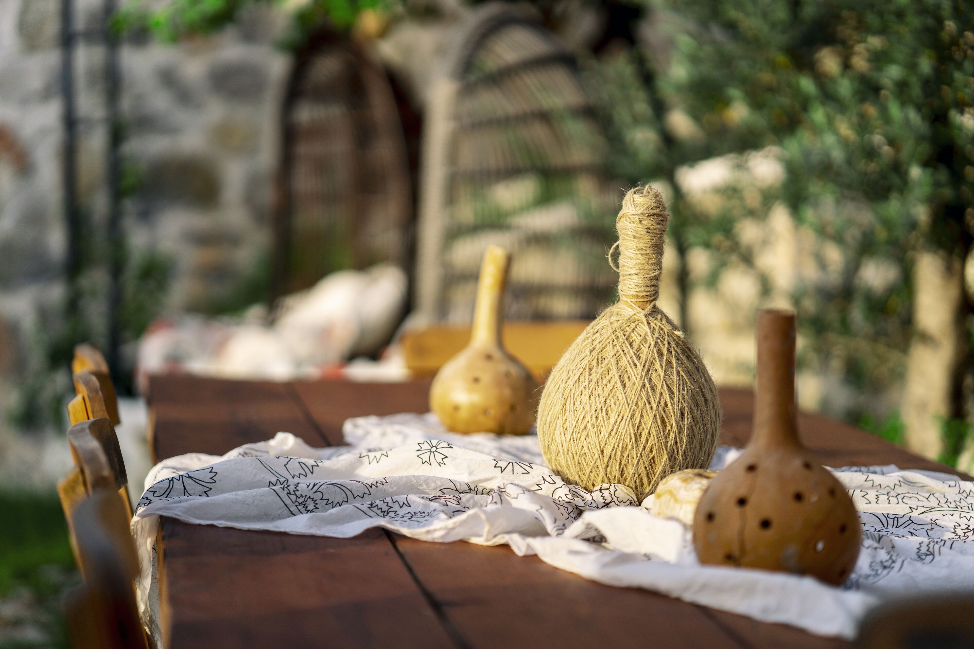 A rustic wooden table with woven baskets and ceramic containers, set outdoors with a stone wall and greenery in the background.