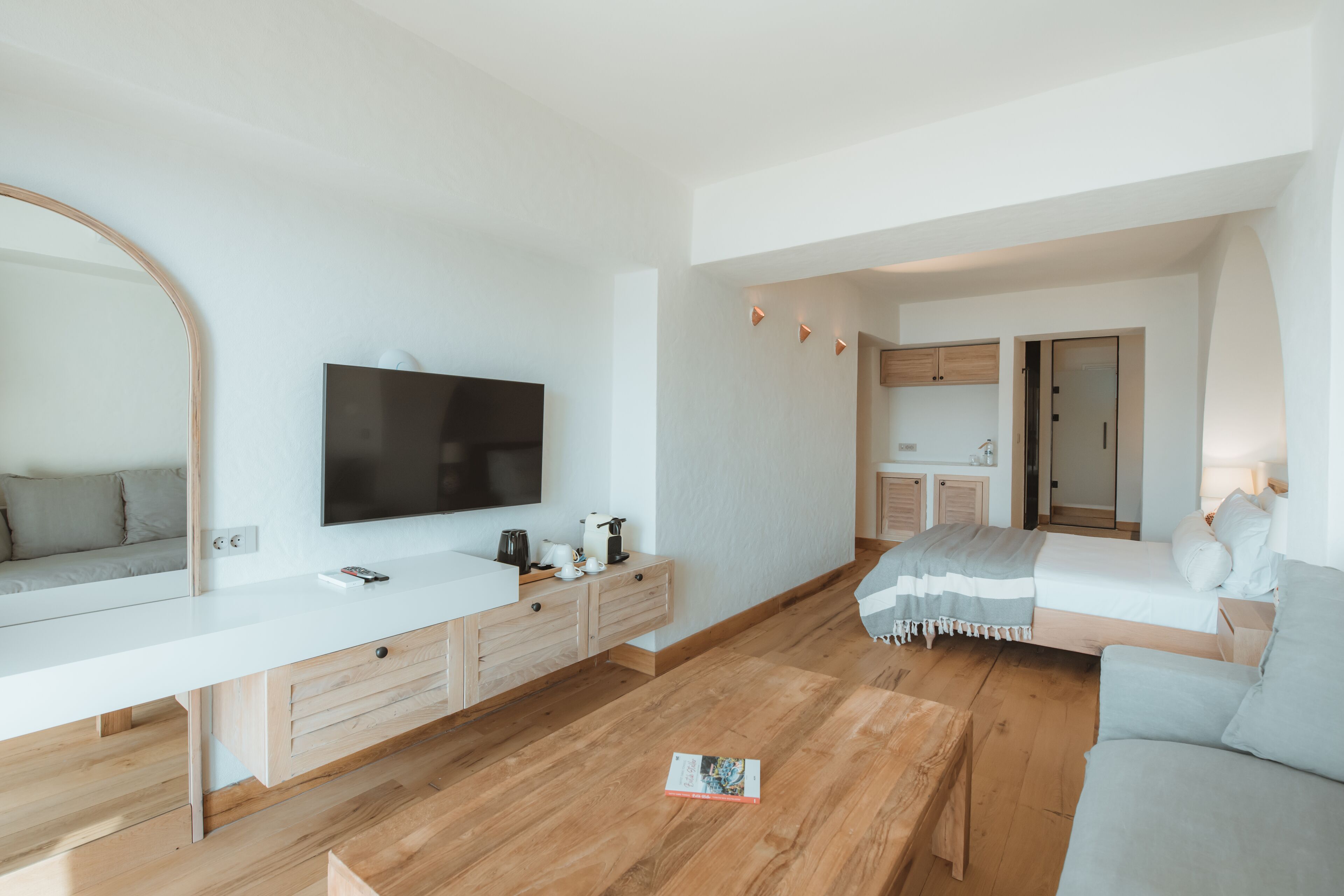 A modern living room with a large flat-screen TV, a wooden coffee table, a sofa, and a dining area with a kitchen in the background.