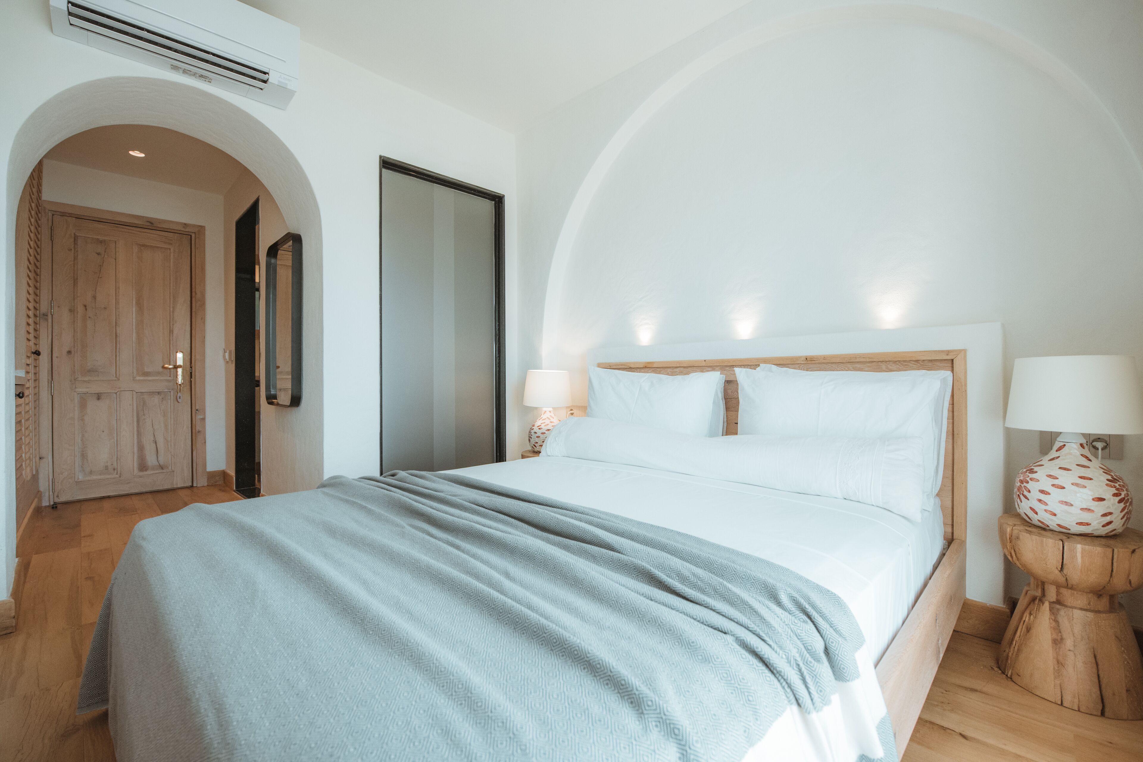 Un dormitorio con una cama, una puerta de madera, un espejo y una lámpara.
