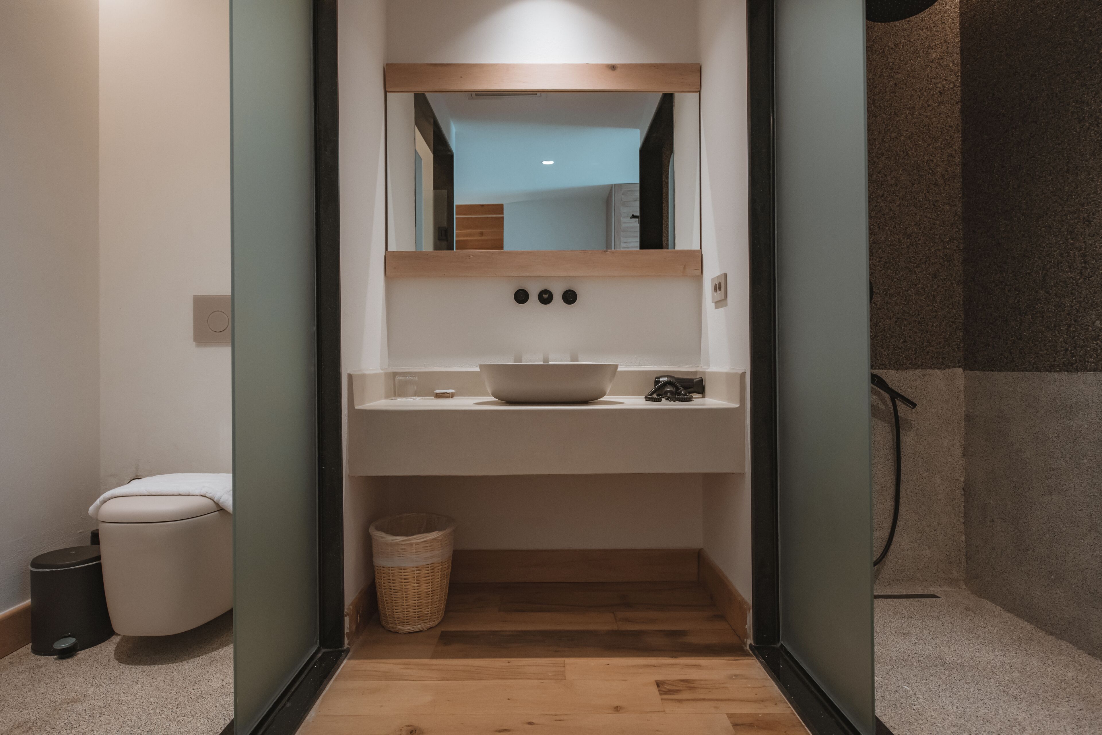 A small, modern bathroom with a wooden floor, a white sink, and a mirror above it.