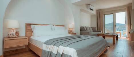 Quarto moderno com uma cama grande, mesas de cabeceira de madeira, um sofá e vista para o exterior.