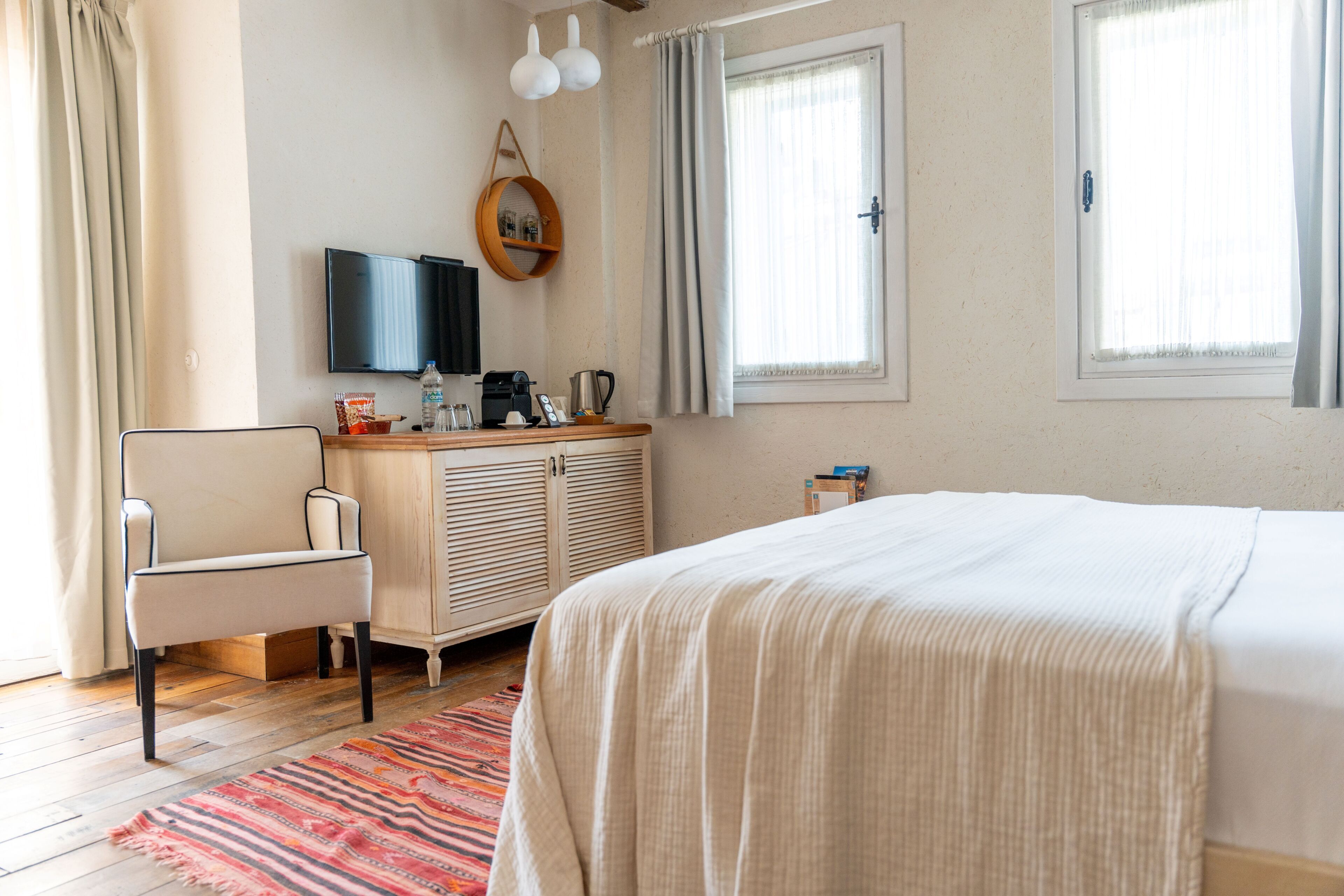 A bedroom with a bed, a chair, a dresser, a television, and windows.