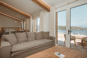 A modern living room with a sofa, wooden coffee table, and a view of a beach and marina through large sliding glass doors.