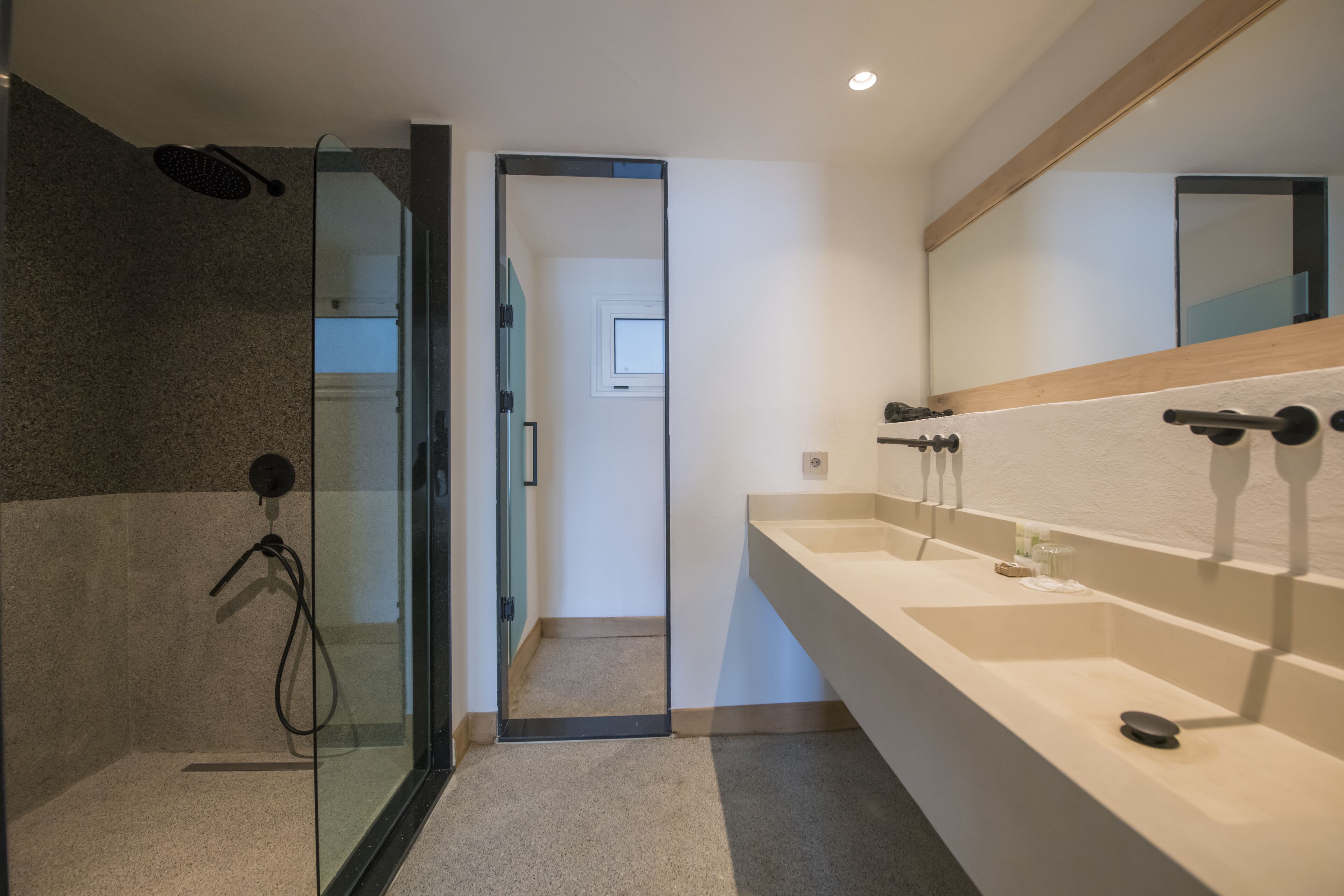 A modern bathroom with a glass shower enclosure, a large mirror, and a beige countertop with two sinks.