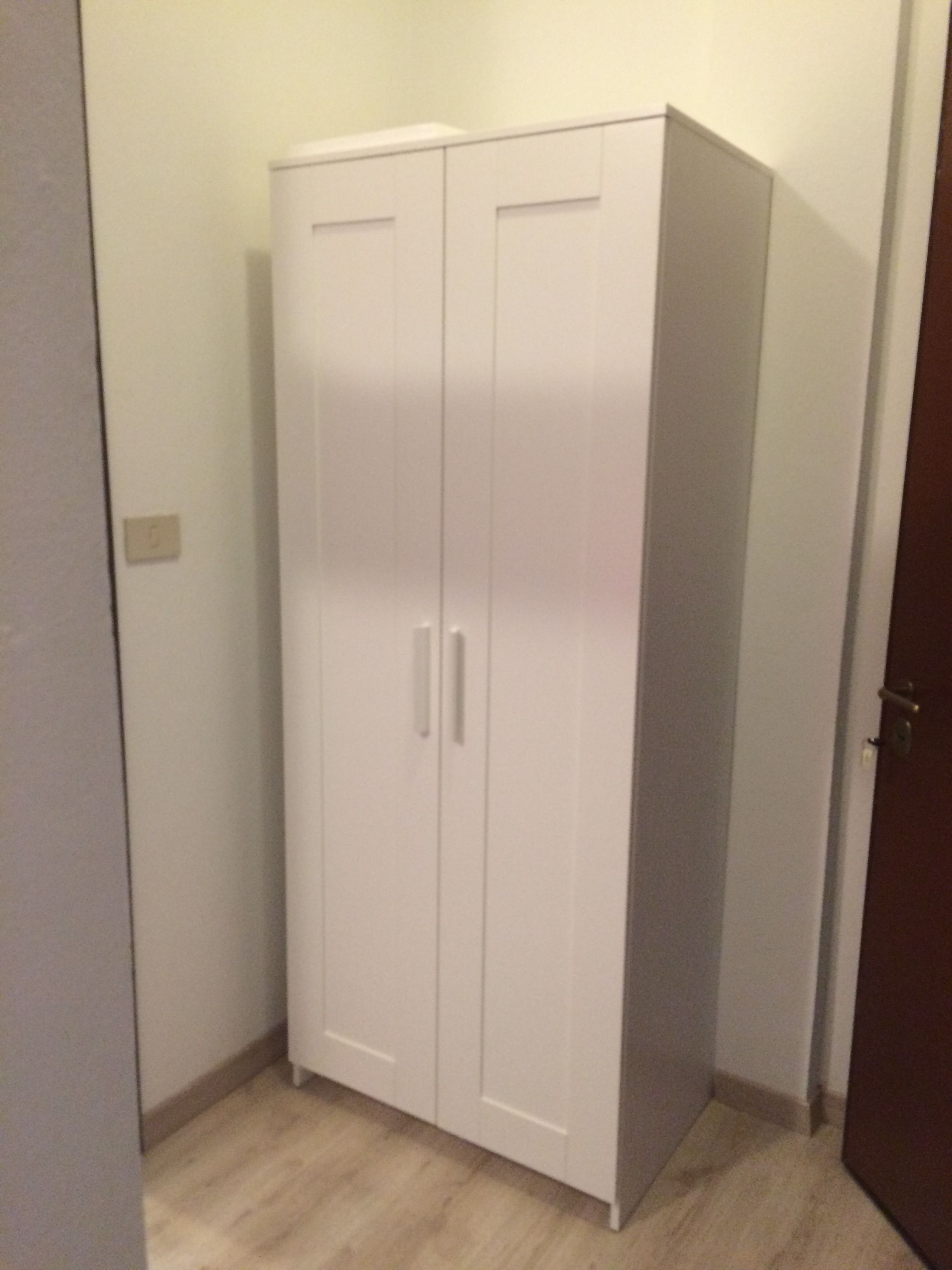 A white wardrobe with two doors and a handle in a room with light-colored wooden flooring.