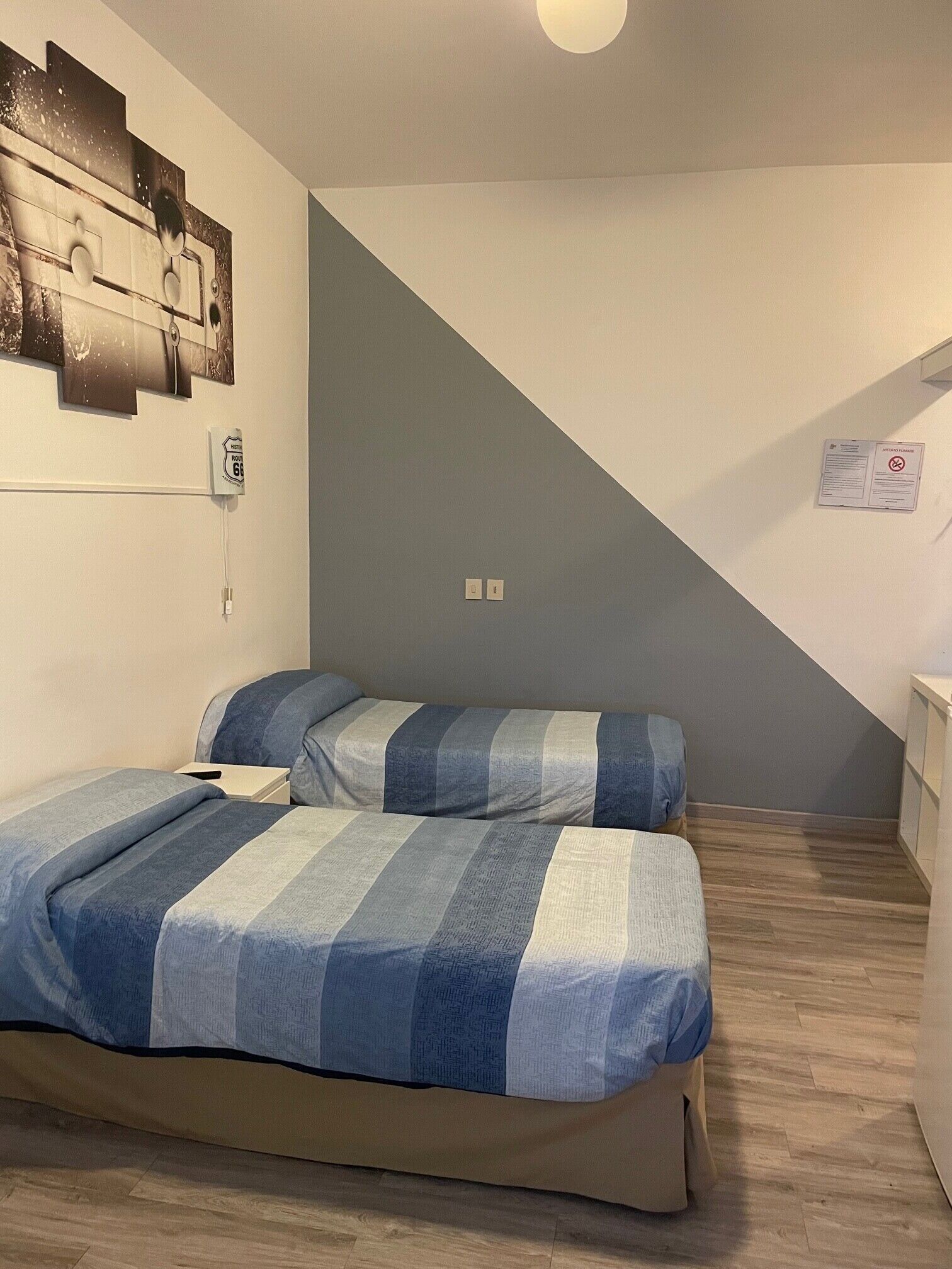 A bedroom with two beds, a wall-mounted light fixture, a power outlet, and a notice on the wall.