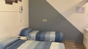 A bedroom with two beds, a wall-mounted light fixture, a power outlet, and a notice on the wall.