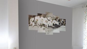 A room with two beds, a ceiling fan, a desk with a lamp, and a wall with a floral artwork.