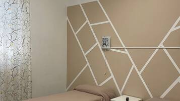 Een hotelkamer met twee eenpersoonsbedden, een plafondventilator, een muur met geometrische patronen en een decoratieve wandversiering.
