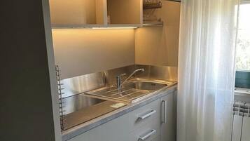 Una cocina moderna con horno empotrado, pileta de acero inoxidable y una ventana con cortinas.