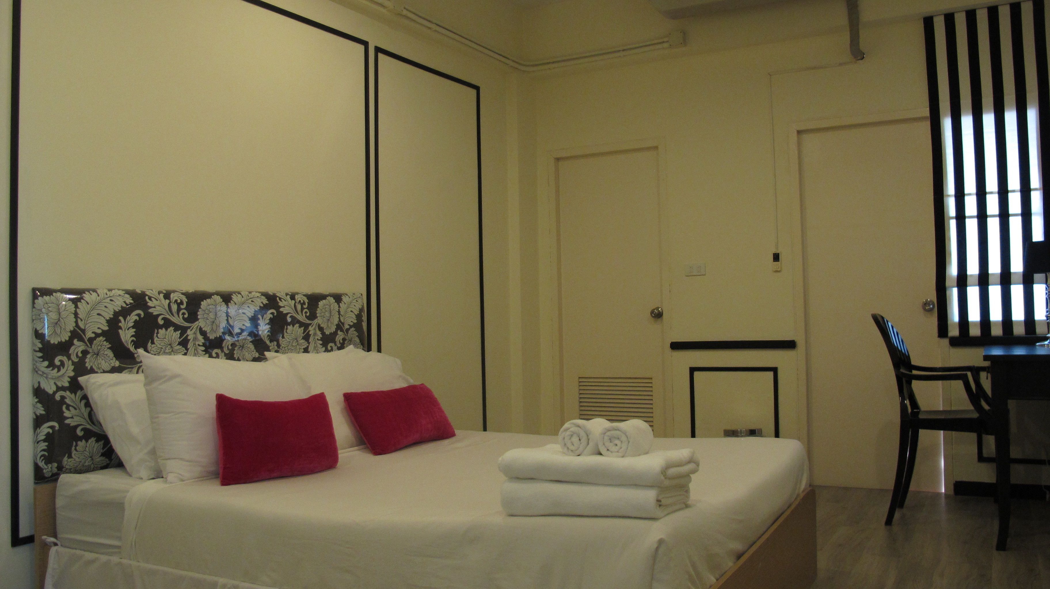 Une chambre d’hôtel avec un lit, deux oreillers rouges, un bureau et une chaise.