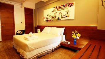 Una habitación de hotel con una cama, una mesita de noche de madera, un florero con flores y una obra de arte en la pared.