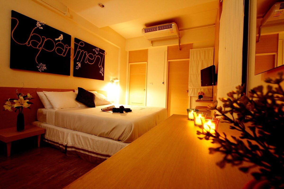 Una habitación de hotel con cama, mesita de noche, lámpara, decoración en la pared y televisor.