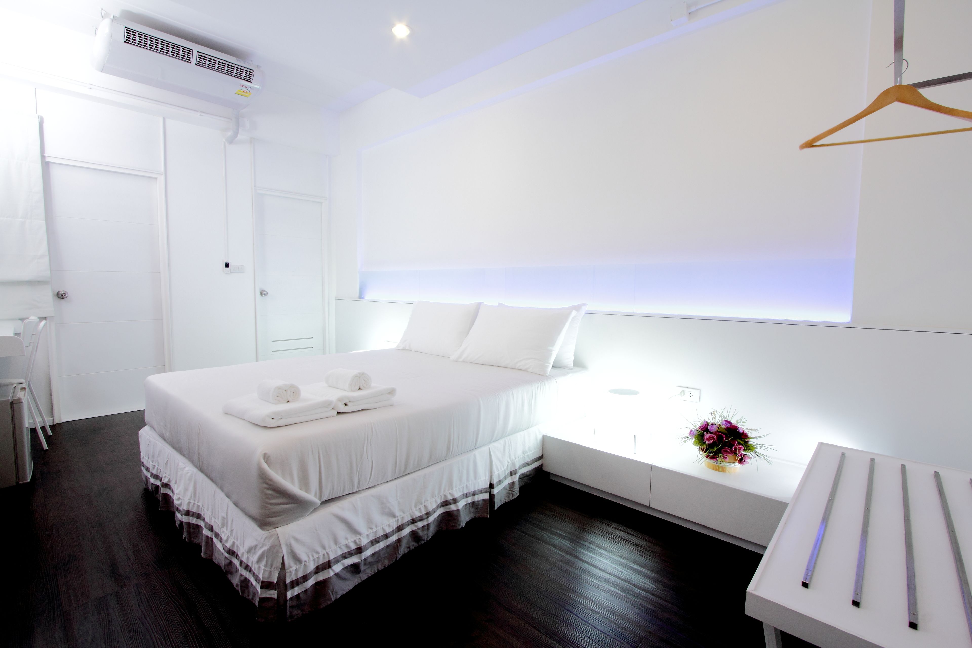 Una habitación de hotel moderna con una cama grande, una mesita de noche, una pequeña mesa con un jarrón de flores y una pared blanca con ventana.