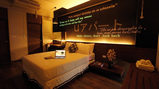 A hotel room with a bed, a laptop, a bedside table with a plant, and a wall with motivational quotes. - U431 Chaengwattana (Pak Kret)