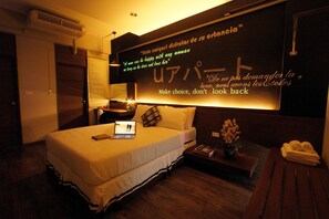 A hotel room with a bed, a laptop, a bedside table with a plant, and a wall with motivational quotes. - U431 Chaengwattana (Pak Kret)