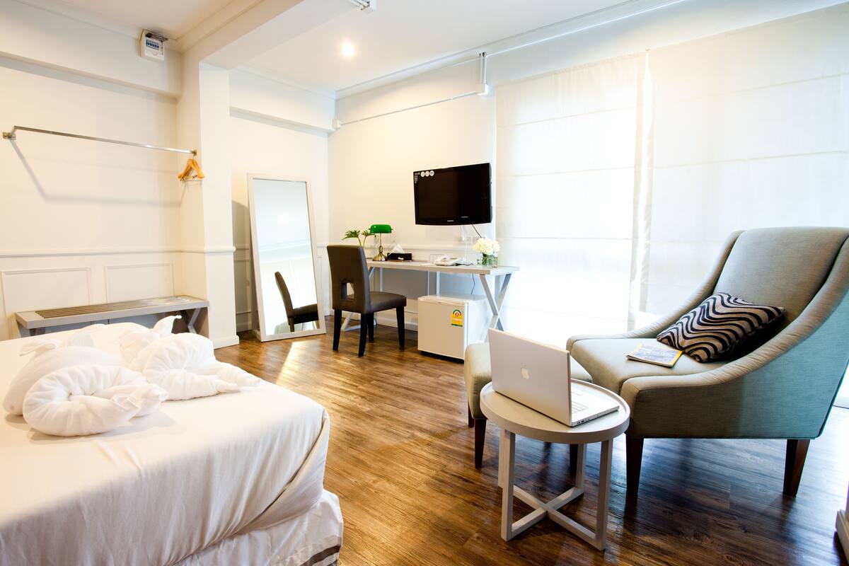 A hotel room with a bed, a desk with a laptop, a chair, and a TV.