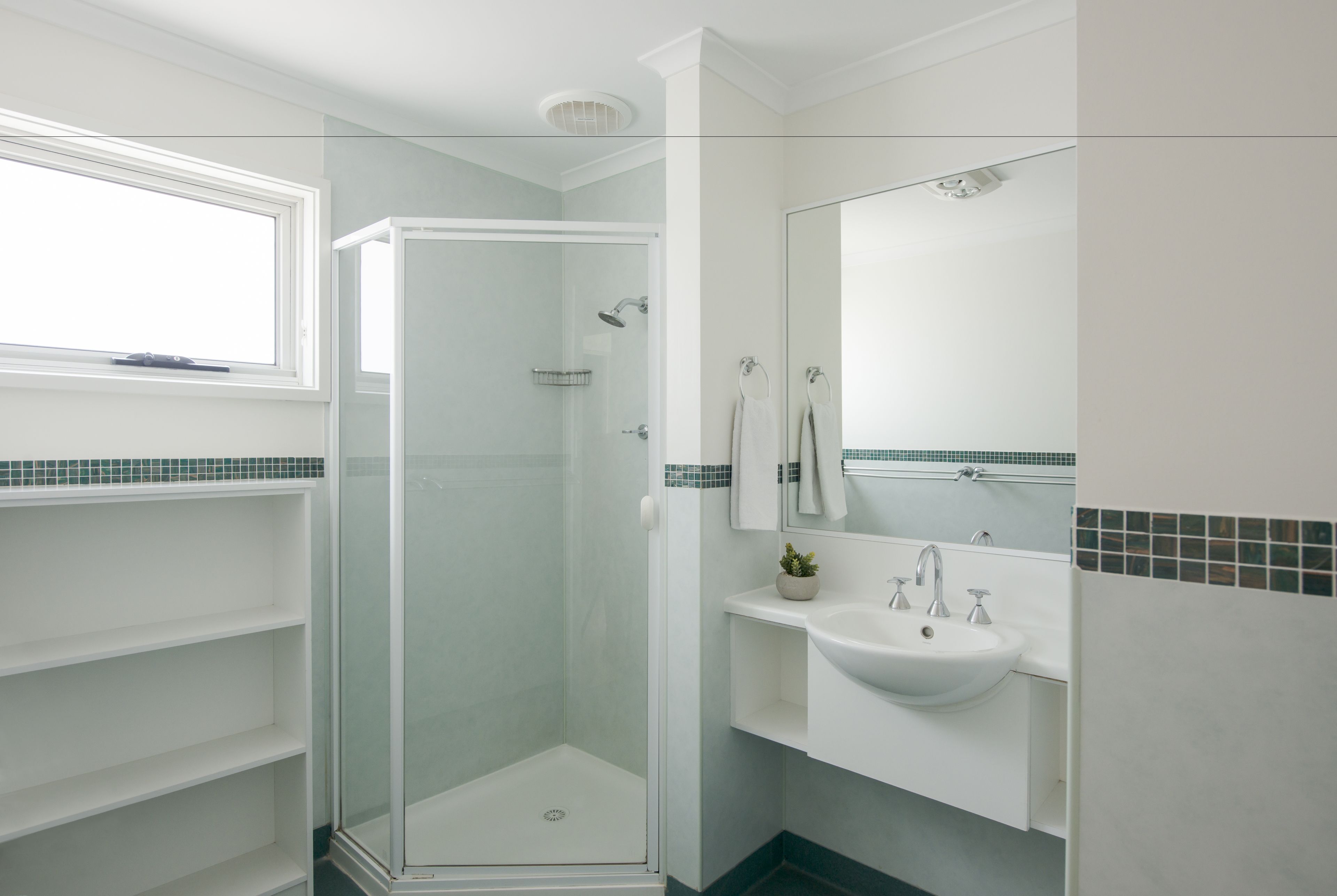 A modern bathroom with a glass-enclosed shower, a white sink, and a mirror above it.