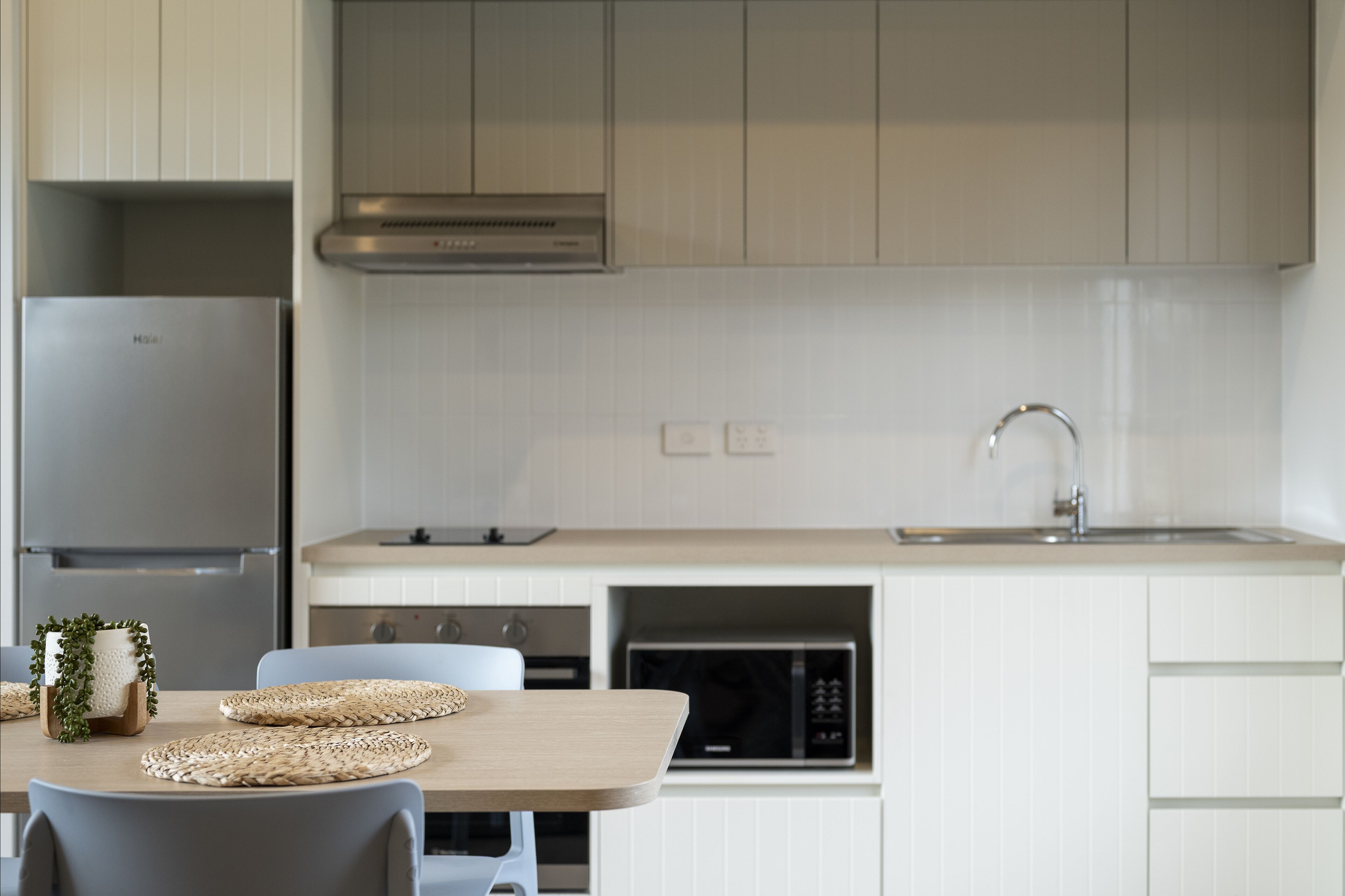 A modern kitchen with white cabinets, a stainless steel refrigerator, a microwave, and a sink with a faucet.