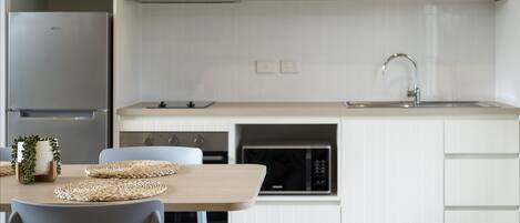 A modern kitchen with white cabinets, a stainless steel refrigerator, a microwave, and a sink with a faucet.