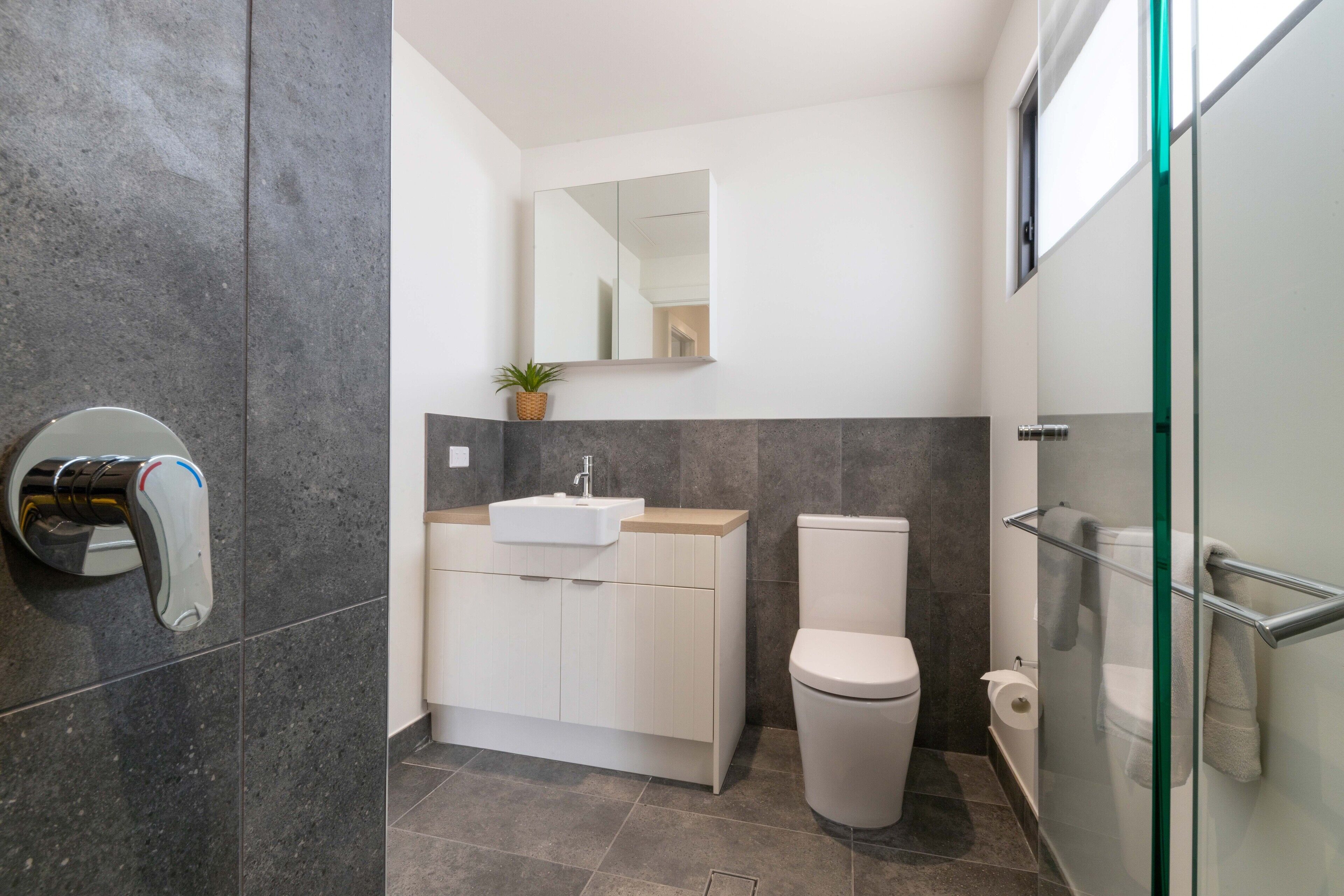 A modern bathroom with a glass shower enclosure, a toilet, and a sink with a mirror above.