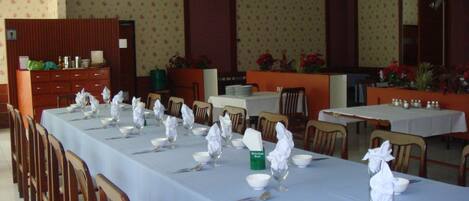 Un comedor con largas mesas dispuestas para varios comensales, con manteles blancos, cubiertos y cristalería.