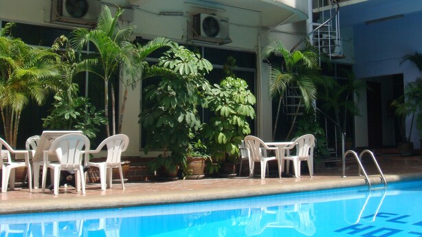 A swimming pool with a white railing, surrounded by potted plants and white plastic chairs. - Florida Hotel (Bangkok)