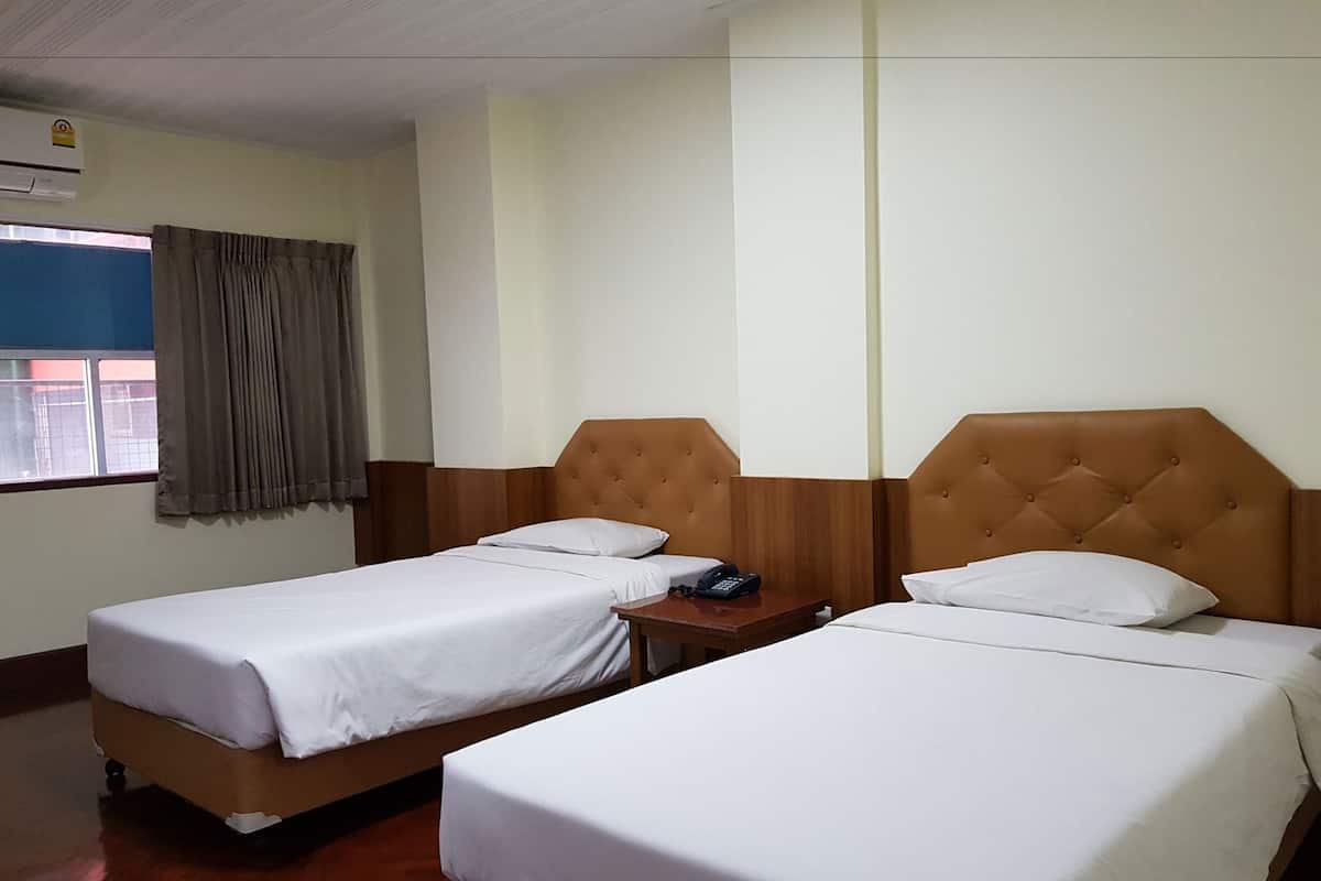 Una habitación de hotel con dos camas individuales, una mesita de noche pequeña con un teléfono, una ventana con cortinas y un equipo de aire acondicionado.