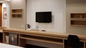 A hotel room with a bed, a desk with a flat-screen TV, a refrigerator, and a chair. - Florida Hotel (Bangkok)