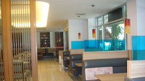 A restaurant interior with booths and tables, a large window, and a decorative light fixture. - Florida Hotel (Bangkok)