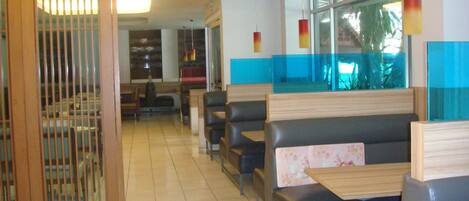 A restaurant interior with booths and tables, a large window, and a decorative light fixture.