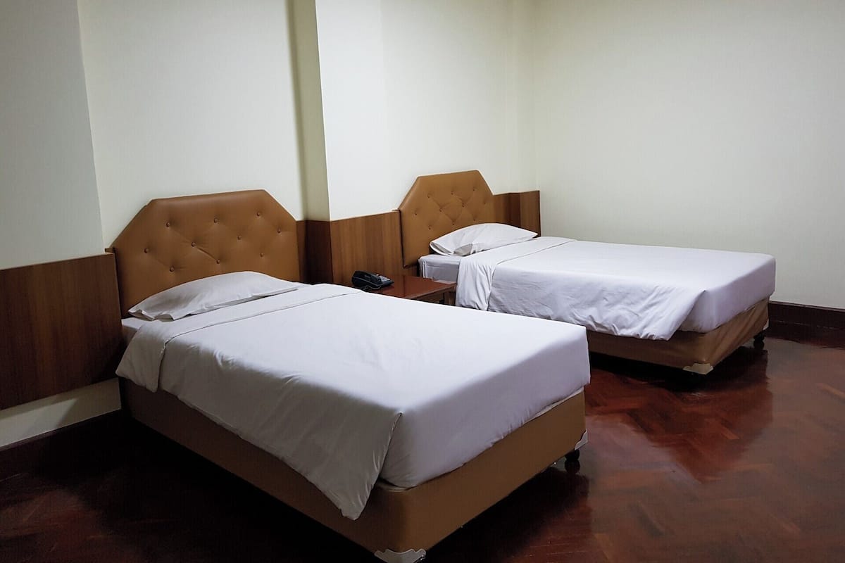 Dos camas individuales con cabeceros de madera y ropa de cama blanca en una habitación con suelo de madera y paredes blancas.