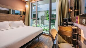 Habitación de hotel con una cama grande, un escritorio con cafetera y vistas a zonas verdes por las ventanas.