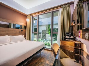 Habitación de hotel con una cama grande, un escritorio con cafetera y vistas a zonas verdes por las ventanas.