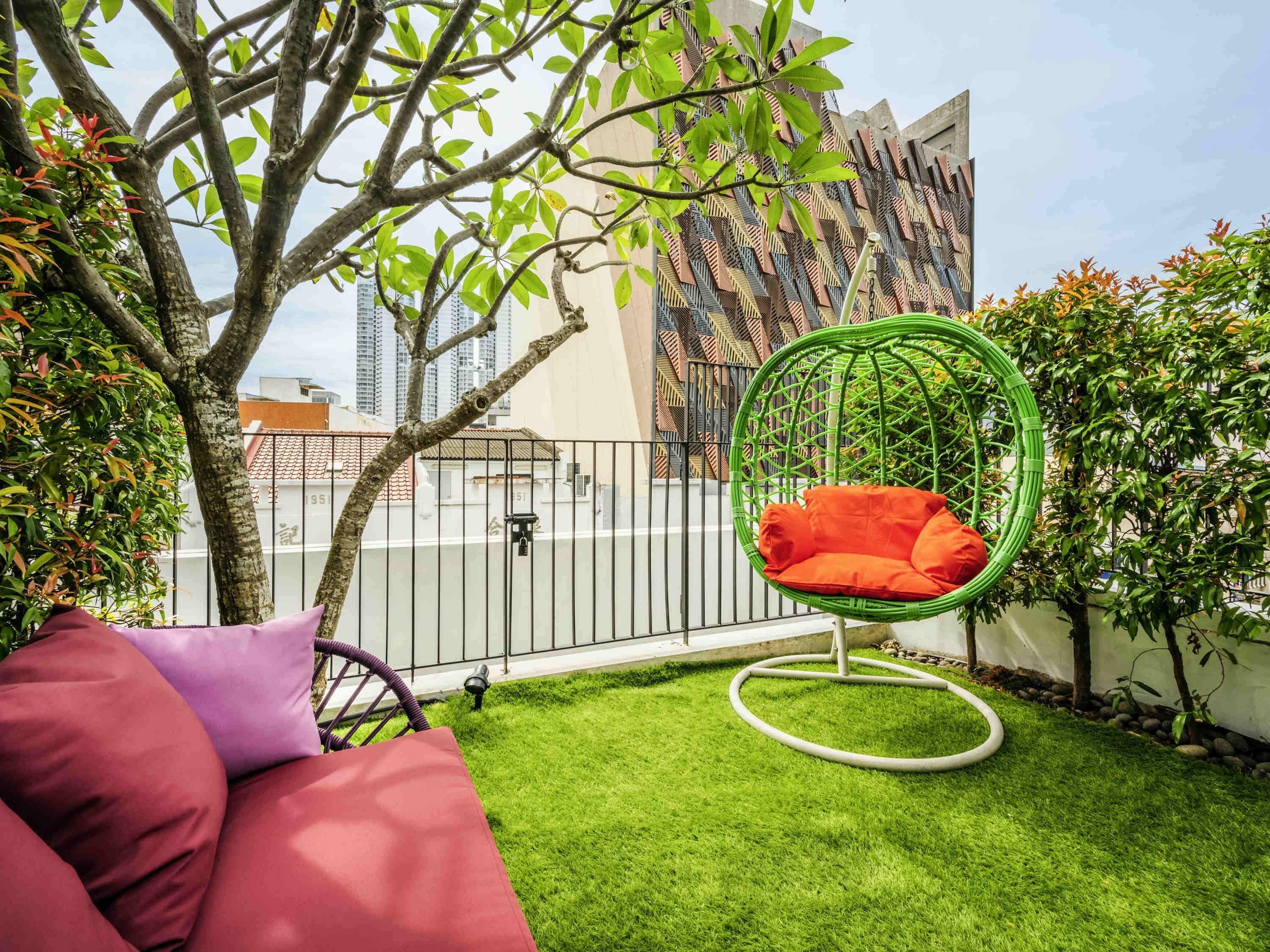 A balcony with a green hanging chair, a red cushion, and a small patch of artificial grass.