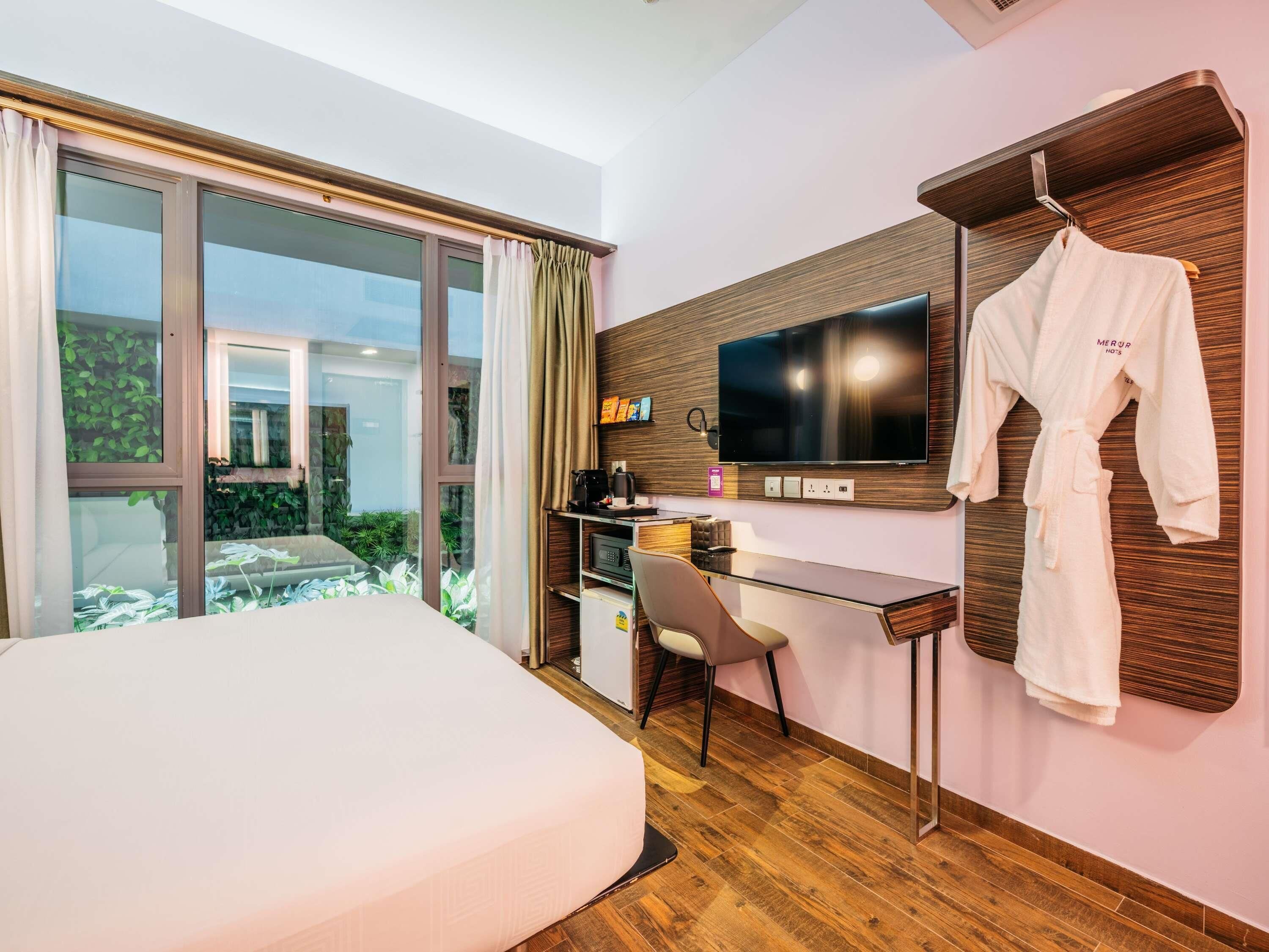 Hotelkamer met een bed, een bureau met een computer, een televisie en een badjas hangend aan een houten paneel.