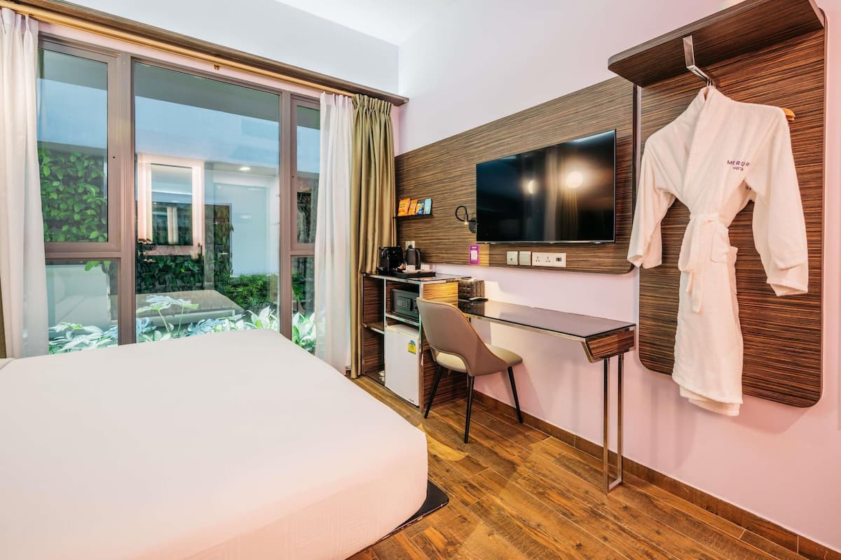 A hotel room with a bed, a desk with a computer, a TV, and a robe hanging on a wooden panel.