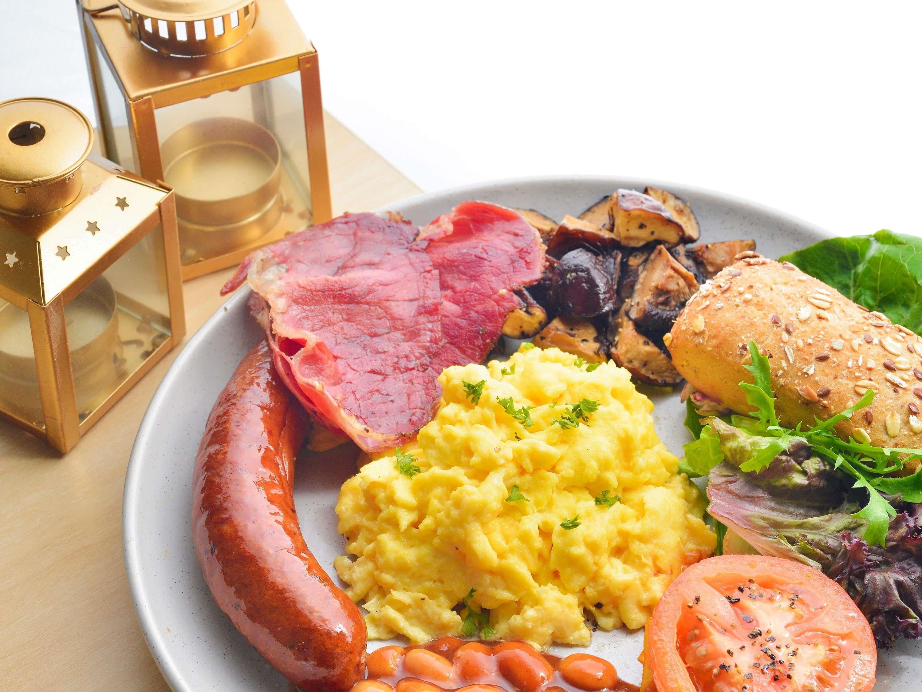 A plate with a sausage, ham, mushrooms, scrambled eggs, and a sandwich.