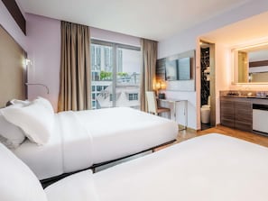 A hotel room with two beds, a desk, a TV, and a bathroom.