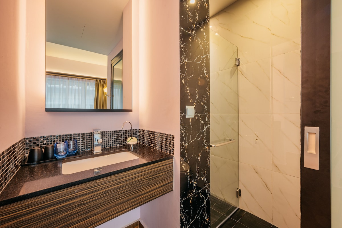 A modern bathroom with a dark marble wall, a black countertop, and a glass shower enclosure.