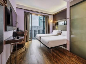 Une chambre d’hôtel avec un lit, un bureau, une chaise, une télévision et un balcon avec des rideaux.