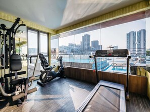 Un gimnasio con equipo de cardio, una máquina de remo y una cinta de correr. Cuenta con grandes ventanales y vistas a la ciudad.