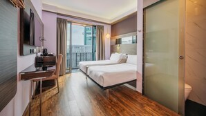 Una habitación de hotel moderna con escritorio, dos camas, un balcón y una puerta corrediza.
