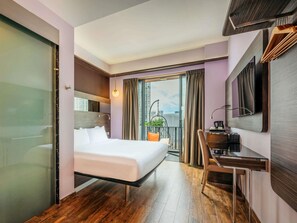 Een hotelkamer met een bed, bureau en uitzicht op de stad.