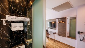 Baño de hotel con pared de mármol negro, un lavamanos y un perchero con toallas del hotel Mercure.