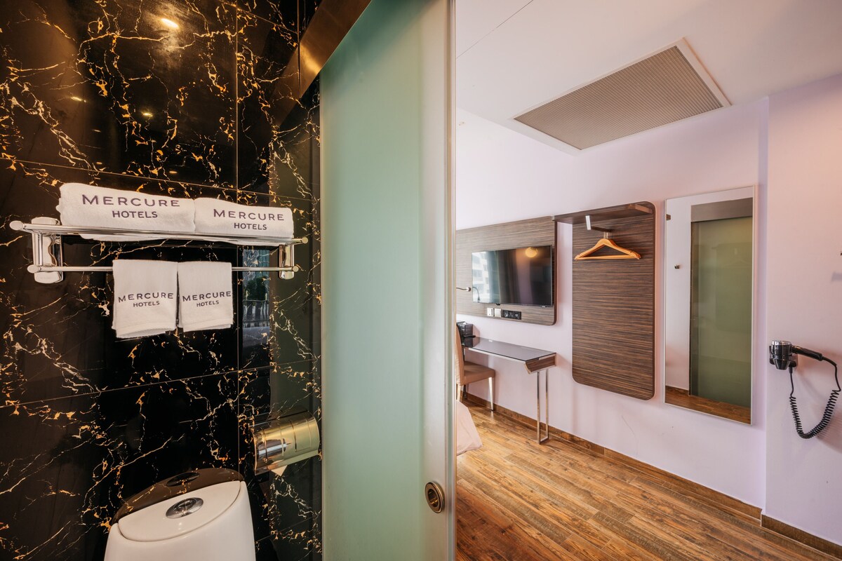 A hotel bathroom with a black marble wall, a sink, and a towel rack with 'Mercure Hotels' towels.