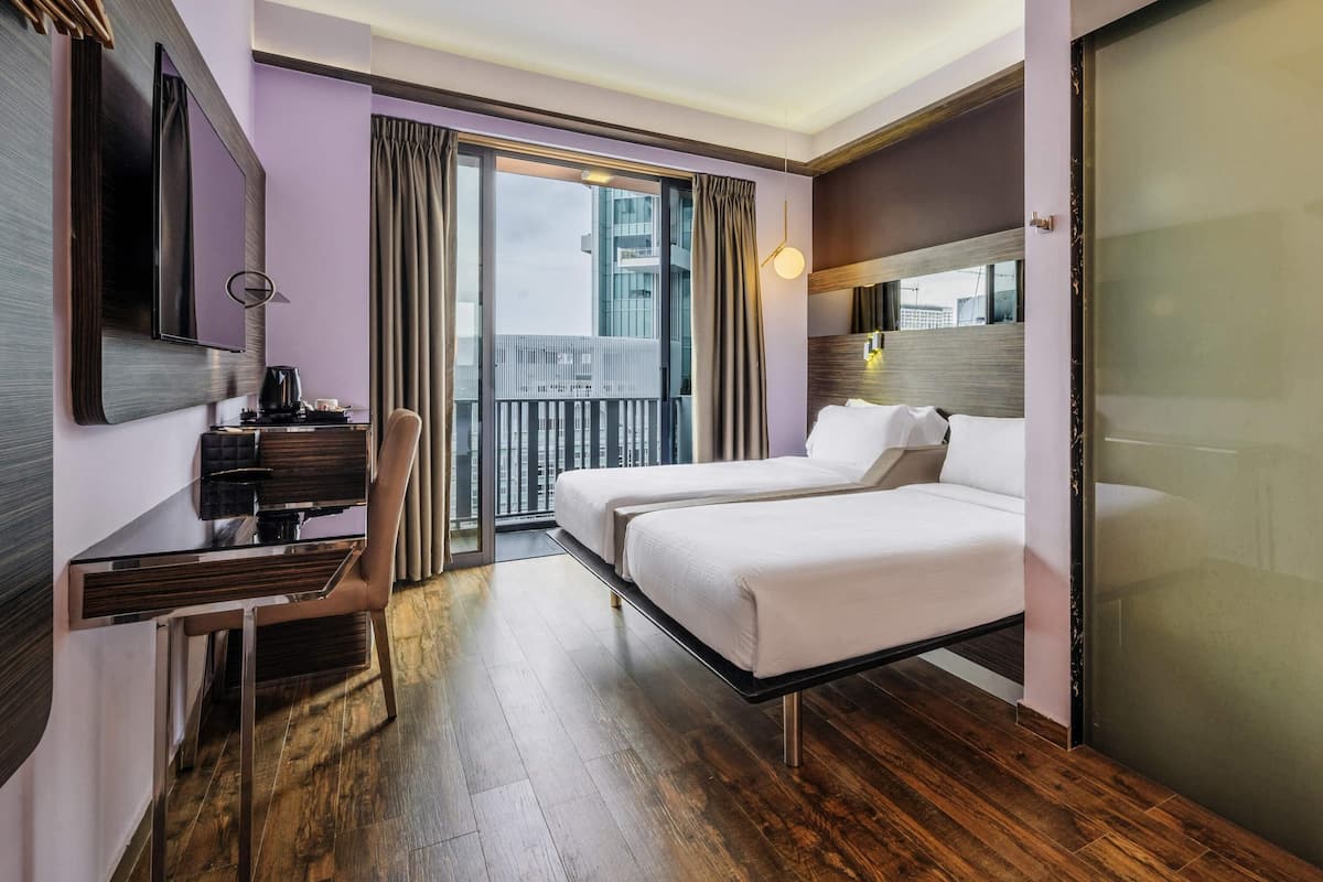 Une chambre d’hôtel avec un lit, un bureau, une chaise, une télévision et un balcon avec des rideaux.