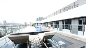 Zona de piscina en la azotea con sillones y una mesa, con vistas a un paisaje urbano.